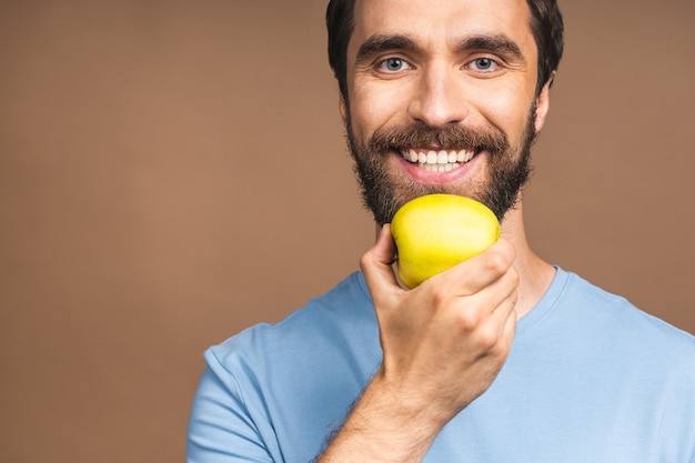 Conceito de dieta. Alegre linda barbudo jovem comendo maçã verde, isolada sobre fundo bege.