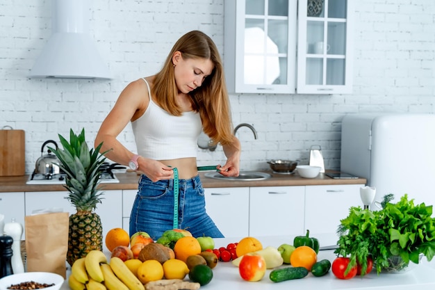 Conceito de dieta Fêmea na cozinha com alimentos saudáveis Frutas e legumes Fita métrica na cintura