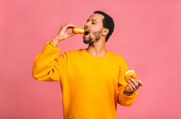 Conceito de dieta. Homem barbudo com fome comendo rosquinhas isoladas em rosa.