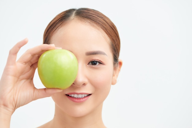 Conceito de dieta saudável. Mulher jovem sorridente atraente segurando maçã verde fresca cobrindo os olhos no café da manhã em branco