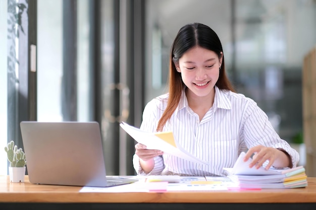 Conceito de documentos de negócios Mãos de mulher de funcionário trabalhando em arquivos de papel de pilhas para pesquisar e verificar documentos inacabados alcança em papéis de pastas no escritório de mesa de trabalho ocupado Foco suave