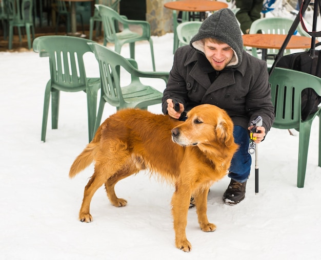 Conceito de dono, cachorro e pessoas do animal de estimação - jovem sorridente homem caucasiano e cachorro ao ar livre no inverno.