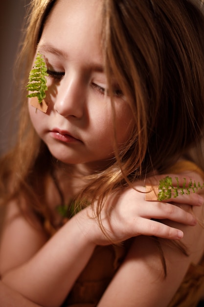 Conceito de ecologia e vacinação, retrato de uma menina com ramos de samambaia colados com curativo na bochecha e no dedo