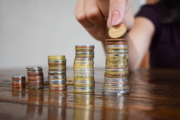 Foto conceito de economia de dinheiro, predefinido pela mão feminina, colocando dinheiro da pilha de moedas.