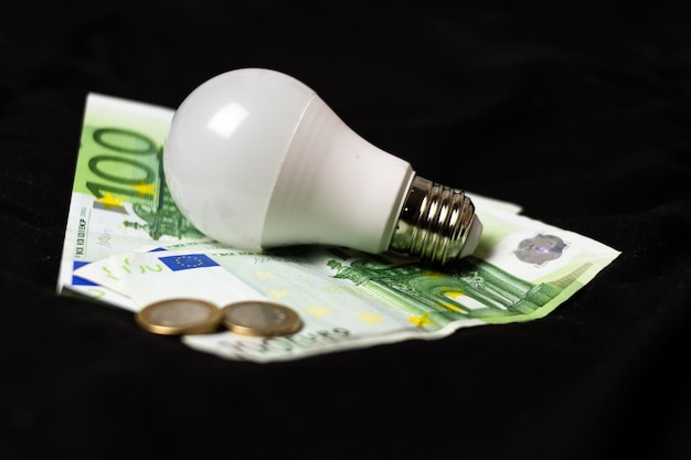 Conceito de economia de luz e dinheiro lâmpada elétrica em dinheiro e moedas Finanças e economia de eletricidade