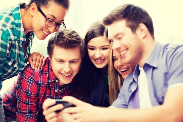 conceito de educação e internet - alunos sorridentes olhando para smartphone na escola