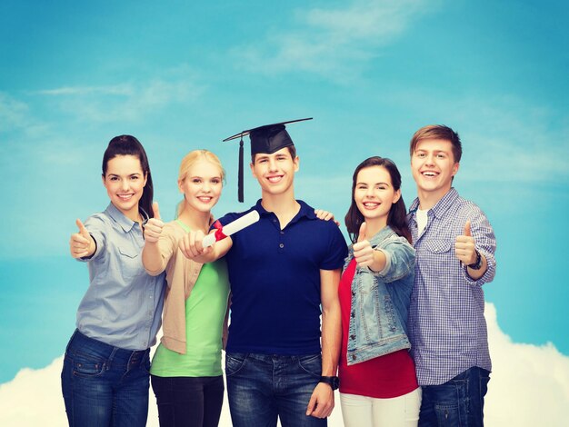 Conceito de educação e pessoas - grupo de estudantes em pé sorrindo com diploma e tampa mostrando os polegares para cima