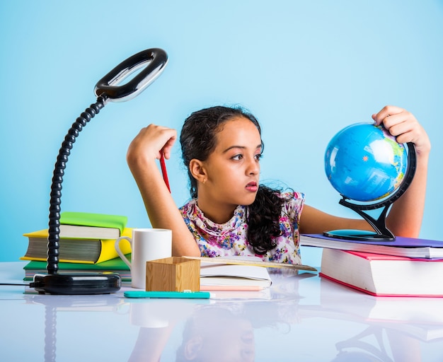 Conceito de educação em casa - linda menina indiana ou asiática estudando em casa com pilha de livros, globo educacional etc. Foco seletivo