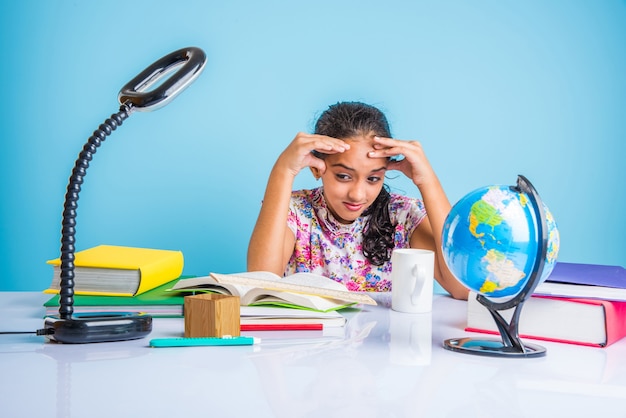 Conceito de educação em casa - linda menina indiana ou asiática estudando em casa com pilha de livros, globo educacional etc. Foco seletivo