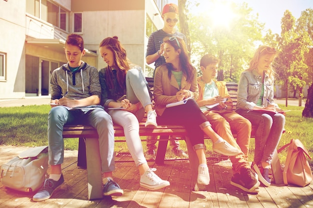 conceito de educação, ensino médio e pessoas - grupo de estudantes adolescentes felizes com cadernos aprendendo no pátio do campus