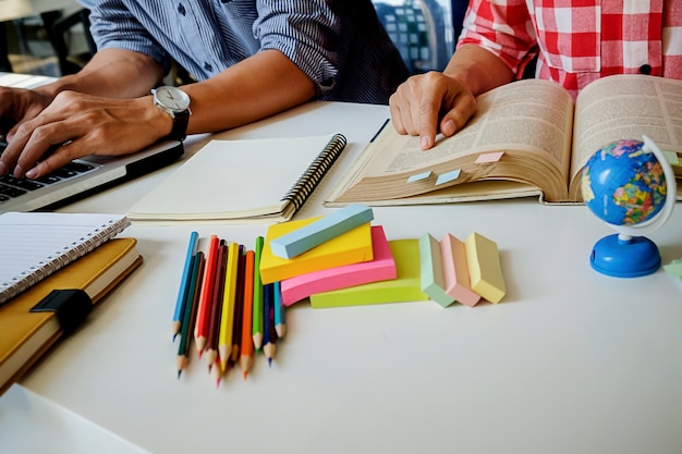 Conceito de educação. Estudantes que estudam e fazem o brainstorming do conceito de campus. Feche os alunos discutindo o assunto em livros de livros e escrevendo para o caderno. Foco seletivo.