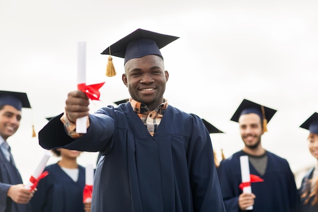 Conceito de educação, graduação e pessoas - grupo de estudantes internacionais felizes em placas de argamassa e vestidos de solteiro com diplomas