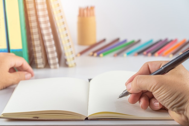 Conceito de educação. mão homem escrever notebook e material escolar na mesa