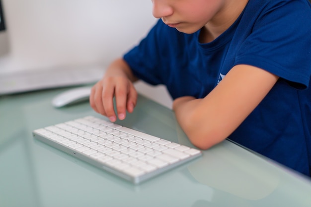 Conceito de educação. menino digitando no teclado do computador e fazendo a lição de casa no pc de mesa