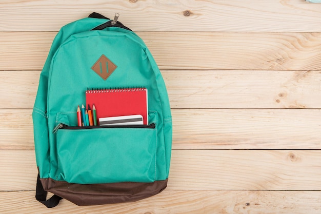 Conceito de educação - mochila azul, cadernos vermelhos e lápis na mesa de madeira