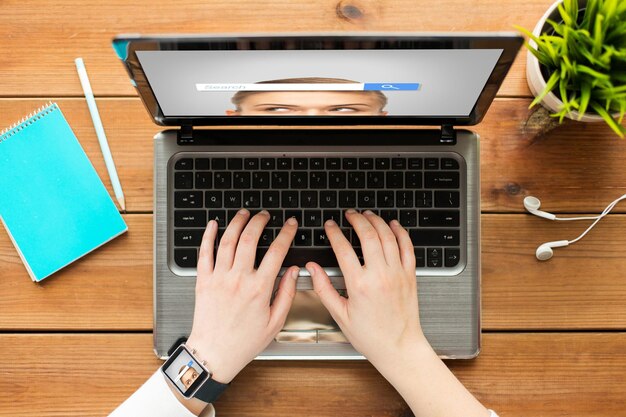 conceito de educação, negócios, pessoas e tecnologia - close-up de mulher ou estudante digitando no computador laptop com barra de pesquisa do navegador de internet na tela, notebook e fones de ouvido na mesa de madeira