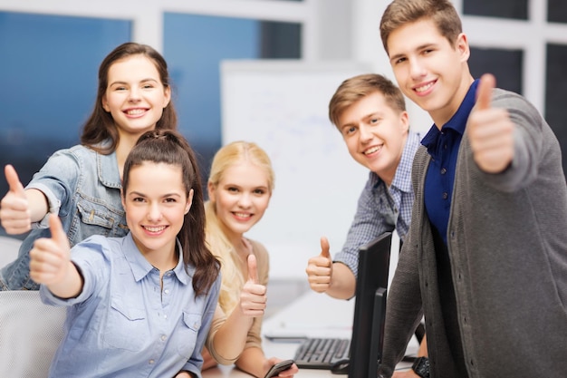 Conceito de educação, tecnologia e internet - grupo de alunos sorridentes com monitor de computador e smartphones