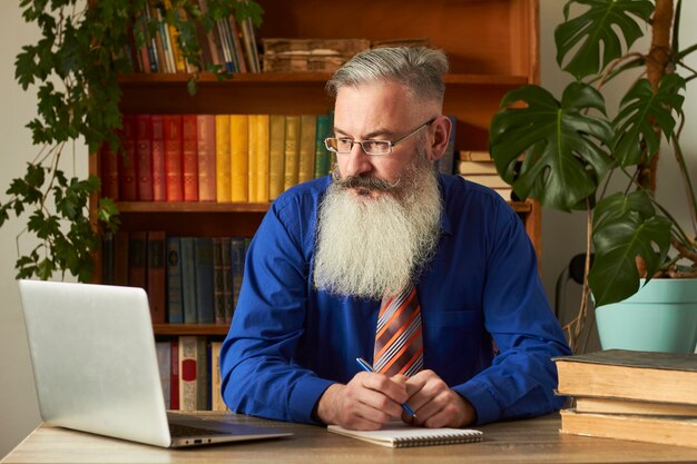 Conceito de ensino a distância. professor professor tutor ensina disciplina online. homem barbudo maduro responde a pergunta do professor através do laptop.