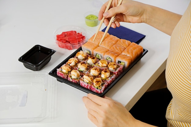 Conceito de entrega de comida de sushi. Mulher comendo pãozinho da Filadélfia em talheres de plástico