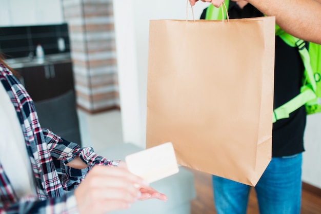 Conceito de entrega de comida. O entregador de comida trouxe comida para casa para a jovem mulher. Ela quer pagar pelo pedido usando o cartão de crédito