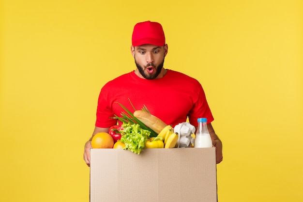 Conceito de entrega de compras online e pedido de comida correio espantado e animado em uniforme vermelho sobre yello ...