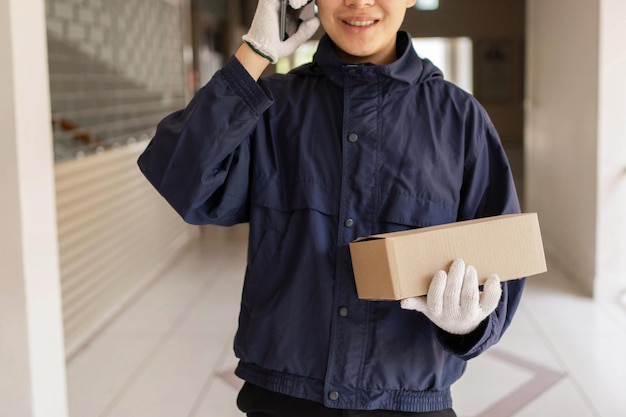 Conceito de entrega de encomendas - o transportador do correio em frente ao prédio ligando para seu cliente