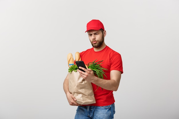 Conceito de entrega: Mensageiro de entrega de mercearia caucasiano bonito uniforme vermelho com caixa de supermercado