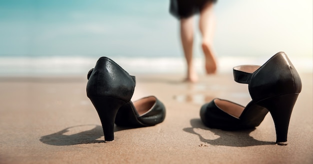 Conceito de equilíbrio de vida profissional. mulher de negócios tira os sapatos de trabalho na praia de areia, caminha até o mar