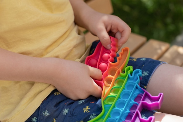 Conceito de equilíbrio emocional Um garotinho brinca com um brinquedo anti-stress pop It Brinquedo anti-stress de silicone sensorial multicolorido pop-lo