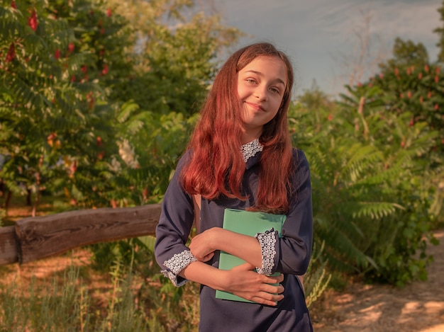 Conceito de escola. Colegial em um vestido de escola com um caderno e uma mochila ao ar livre.