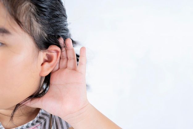 Conceito de escuta A criança asiática apertou a mão perto da orelha e escutou cuidadosamente separadamente em um fundo branco Sintomas de conceitos de perda auditiva