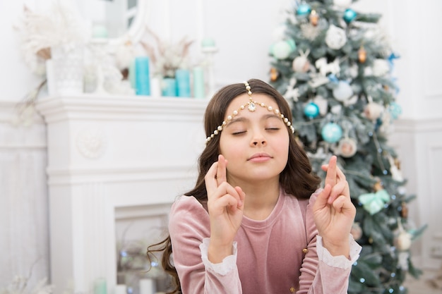 Conceito de esperança. Desejo de Natal de um bebê sonhador. Fazendo desejo. Esperando pelo Papai Noel. Adorável garota fazendo desejo perto do interior decorado da árvore de Natal. Criança esperançosa. Véspera de Ano Novo. Sonhos se tornam realidade.