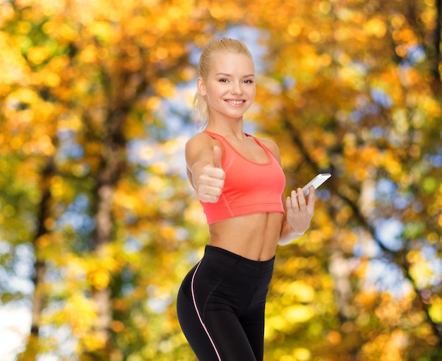 conceito de esporte, fitness, tecnologia, internet e saúde - mulher esportiva sorridente com smartphone mostrando os polegares