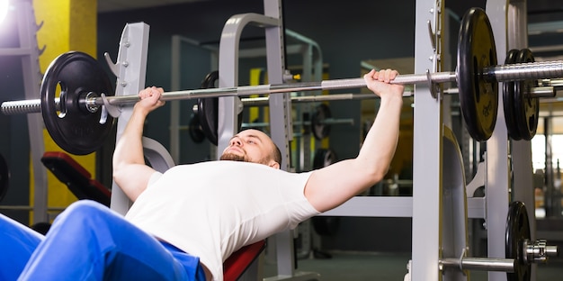 Conceito de esporte, fitness, treinamento e pessoas - homem durante o exercício supino no ginásio.