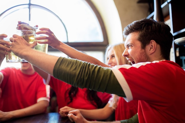 conceito de esporte, futebol, pessoas e lazer - amigos felizes ou fãs de futebol tilintando copos de cerveja no bar ou pub