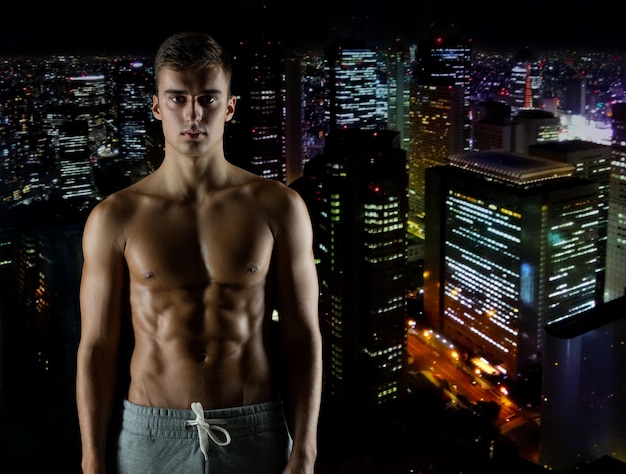 conceito de esporte, musculação, força e pessoas - jovem com torso musculoso nu sobre o fundo da cidade à noite