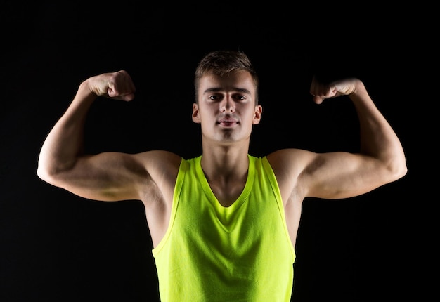 conceito de esporte, musculação, força e pessoas - jovem mostrando bíceps sobre fundo preto