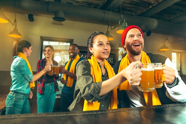 Conceito de esporte, pessoas, lazer, amizade e entretenimento - fãs de futebol felizes ou amigos do sexo masculino bebendo cerveja e comemorando a vitória em um bar ou pub