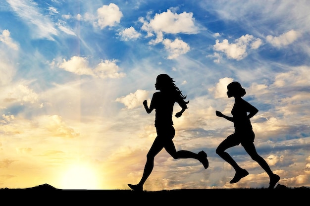 Conceito de esporte. silhueta de duas garotas correndo competição ao pôr do sol