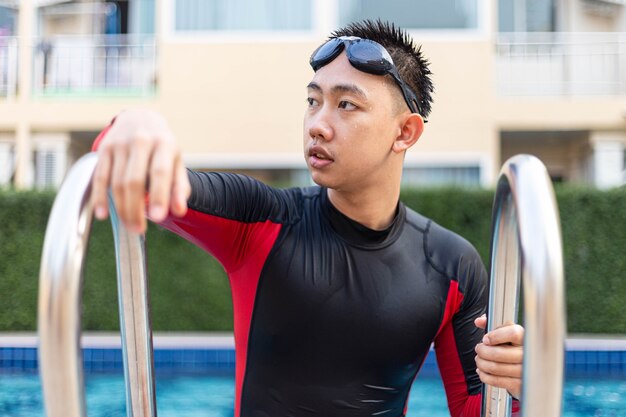 Conceito de esportes e recreação, um adolescente do sexo masculino usando óculos e maiô vermelho e preto saindo da piscina depois de nadar.