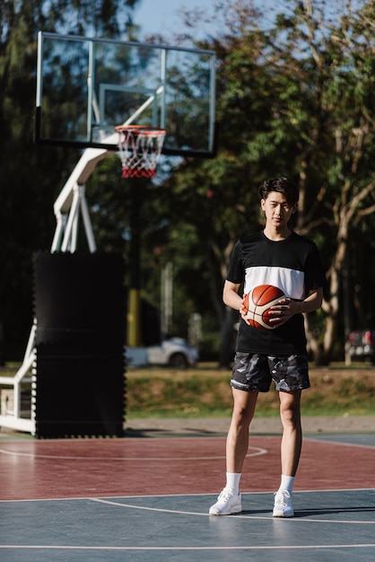 Foto conceito de esportes e recreação, um jovem jogador de basquete masculino segurando uma bola de basquete sozinha no fundo da quadra de basquete.