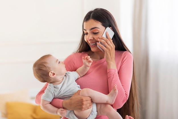 Conceito de estilo de vida da jovem mãe Mãe feliz falando no celular segurando o bebê nos braços e conversando por telefone