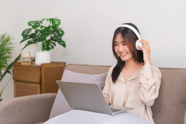 Conceito de estilo de vida de relaxamento A jovem asiática está usando fone de ouvido e assistindo filme no laptop