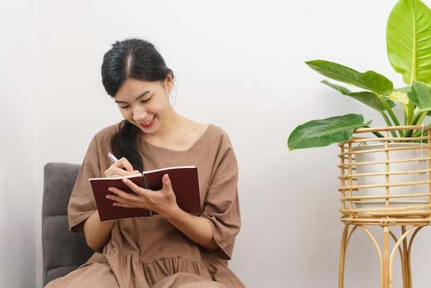 Conceito de estilo de vida de relaxamento jovem asiática escrevendo no notebook enquanto está sentada na sala de estar