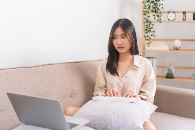 Conceito de estilo de vida de relaxamento Mulher asiática usa teclado para digitar no laptop enquanto trabalha em casa