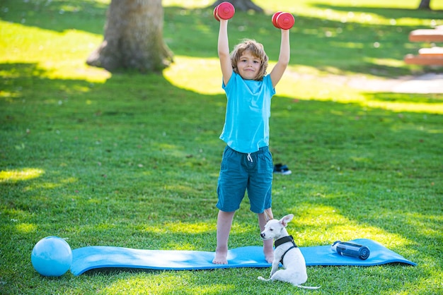 Conceito de estilo de vida desportivo. criança de ioga esporte com haltere e cachorro. rapaz exercitando no parque.