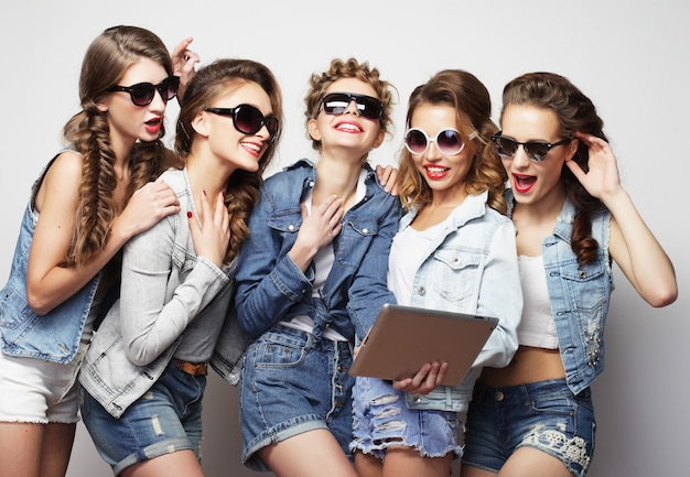 Conceito de estilo de vida e pessoas: cinco amigas hipster tirando selfie com tablet digital, estúdio filmado sobre fundo cinza