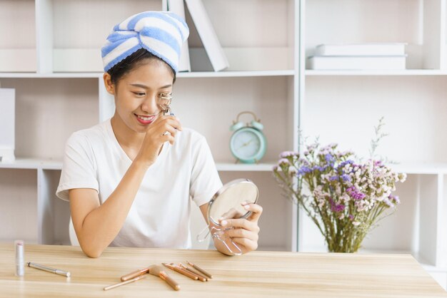 Conceito de estilo de vida em casa Jovem em turbante depois do banho e cílios enrolados para maquiagem em casa