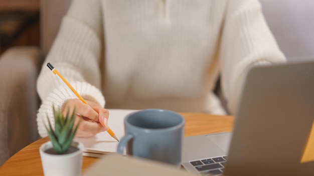 Conceito de estilo de vida em casa Mulher jovem trabalhando em laptop e escrevendo dados em caderno tarde da noite