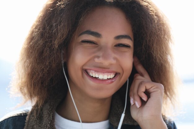 Conceito de estilo de vida Jovem afro-americana usando telefone celular e fones de ouvido sorrindo